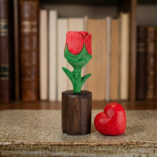 Wooden rose and heart-shaped object on a textured surface with books in the background